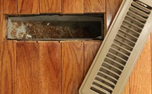 An opened heating/cooling floor vent register showing dirt and debris inside