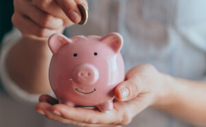 female hands hold a pink piggy bank and puts a coin into the top - saving money on HVAC costs