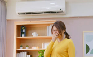 A woman covering her nose while standing near an HVAC unit, reacting to an unpleasant smell. The image highlights the importance of preparing your HVAC system for winter and addressing unusual smells when turning on the heat for the first time.